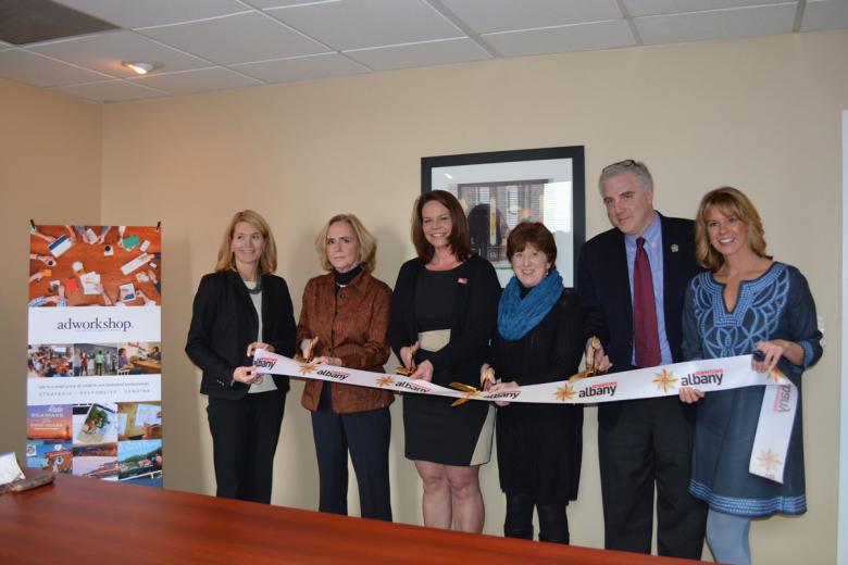 Employees stand with Albany Mayor and BID representatives holding a ribbon for their ribbon cutting ceremony