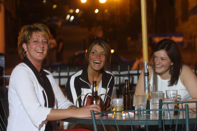 A candid photograph of three women out for drinks, smiling and laughing at the camera and at each other.