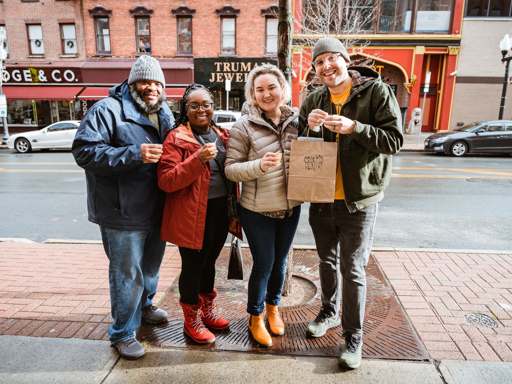 A group of people on Pearl Street smiling with hot chocolate and a shopping bag