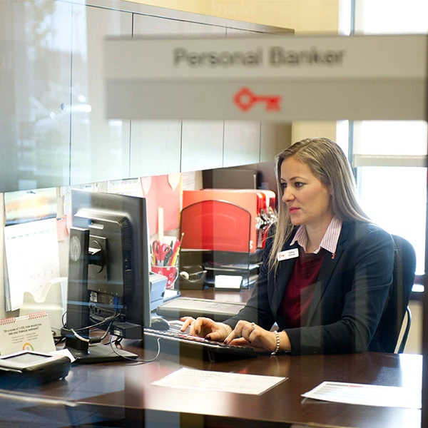 Woman on computer sitting behind glass partition with Key logo and Personal Banker sign