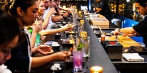 Row of people at left dine on sushi and people at right preparing food