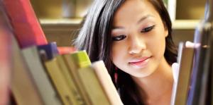 College-age woman looking through books on bookshelf