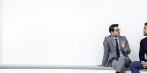 Man in business suit, talking to young man in front of white wall