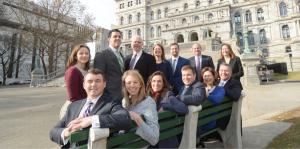 Law firm staff gathered around bench near Capitol building in Albany