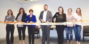 Employees stand with Albany Mayor and BID representatives holding a ribbon for their ribbon cutting ceremony