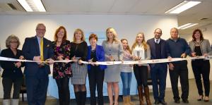 Employees stand with Albany Mayor and BID representatives holding a ribbon for their ribbon cutting ceremony