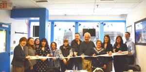 Employees stand with Albany Mayor and BID representatives holding a ribbon for their ribbon cutting ceremony