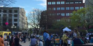 Crowd gathered outside, enjoying foods from various food trucks parked along the street on the left side of the image. 