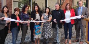 Employees stand with Albany Mayor and BID representatives holding a ribbon for their ribbon cutting ceremony