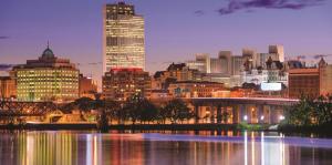 Twilight view of the Albany skyline, building lights reflecting in the still Hudson River in the foreground of the image. 