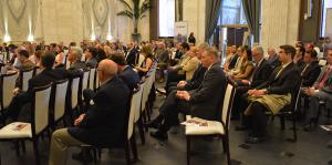 Aisle view of a packed room with rows of chairs filled with business people attending a meeting