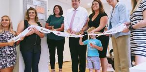 Employees stand with Albany Mayor and BID representatives holding a ribbon for their ribbon cutting ceremony