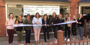 Employees stand with Albany Mayor and BID representatives holding a ribbon for their ribbon cutting ceremony