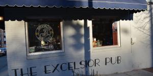 Exterior shot of the Excelsior Pub building, blue awning over the entrance with the logo painted on the building. 