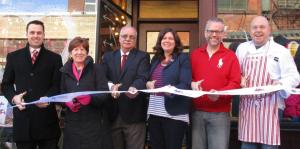 Employees stand with Albany Mayor and BID representatives holding a ribbon for their ribbon cutting ceremony