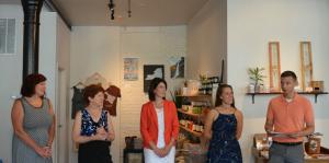 5 store employees stand in an empty back part of the store, addressing the crowd that came to welcome them on their grand opening