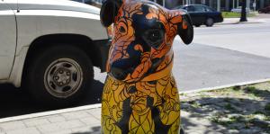 Orange and yellow gradient painted Nipper dog statue with black ink swirl accents sits on the sidewalk in the sun