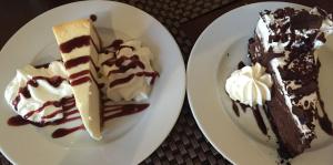 Two plates with decadent slices of cheesecake on each, drizzled with syrups and whipped cream