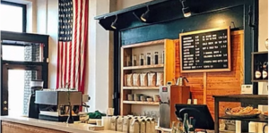 Interior of a business, looking at the counter with the register. A large american flag is hung from the wall near the front door. 