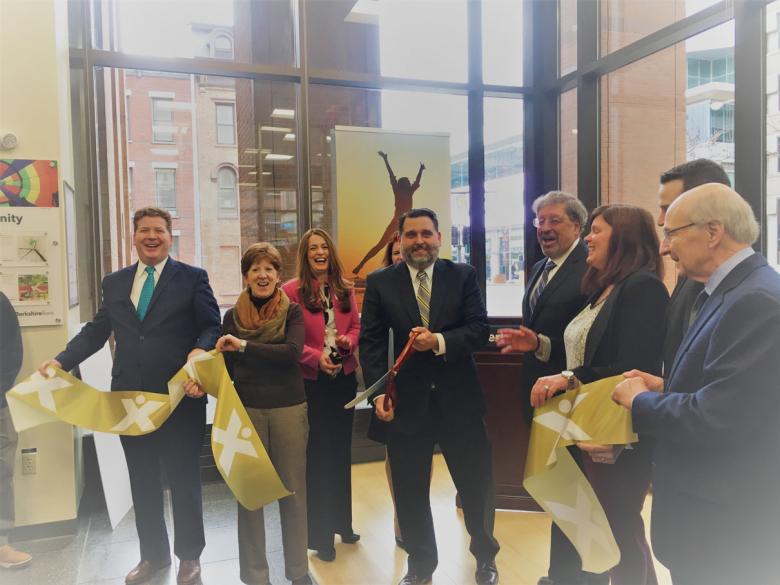 Employees stand with Albany Mayor and BID representatives holding a ribbon for their ribbon cutting ceremony