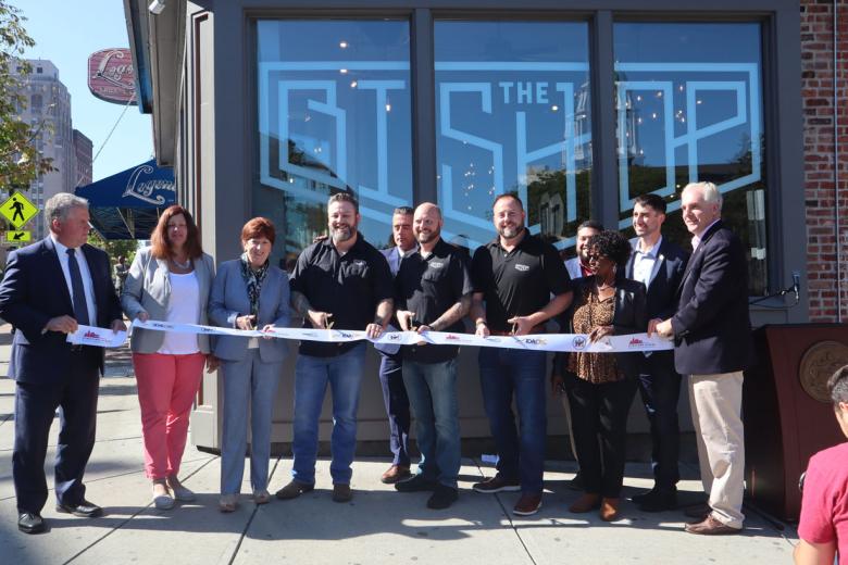 Employees stand with Albany Mayor and BID representatives holding a ribbon for their ribbon cutting ceremony