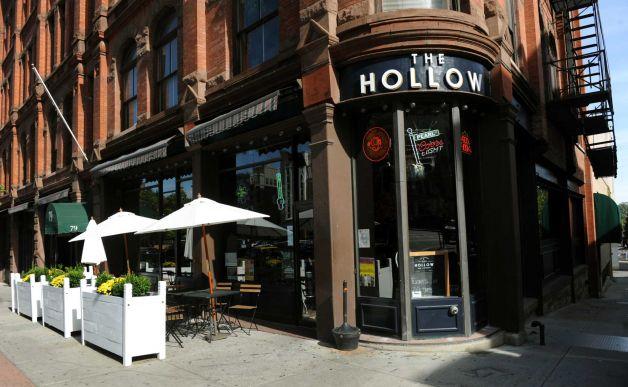 Exterior view of the Hollow restaurant, showing the patio to the left and the front door and main entrance sign to the center. 