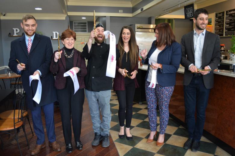 Employees stand with Albany Mayor and BID representatives holding a ribbon for their ribbon cutting ceremony