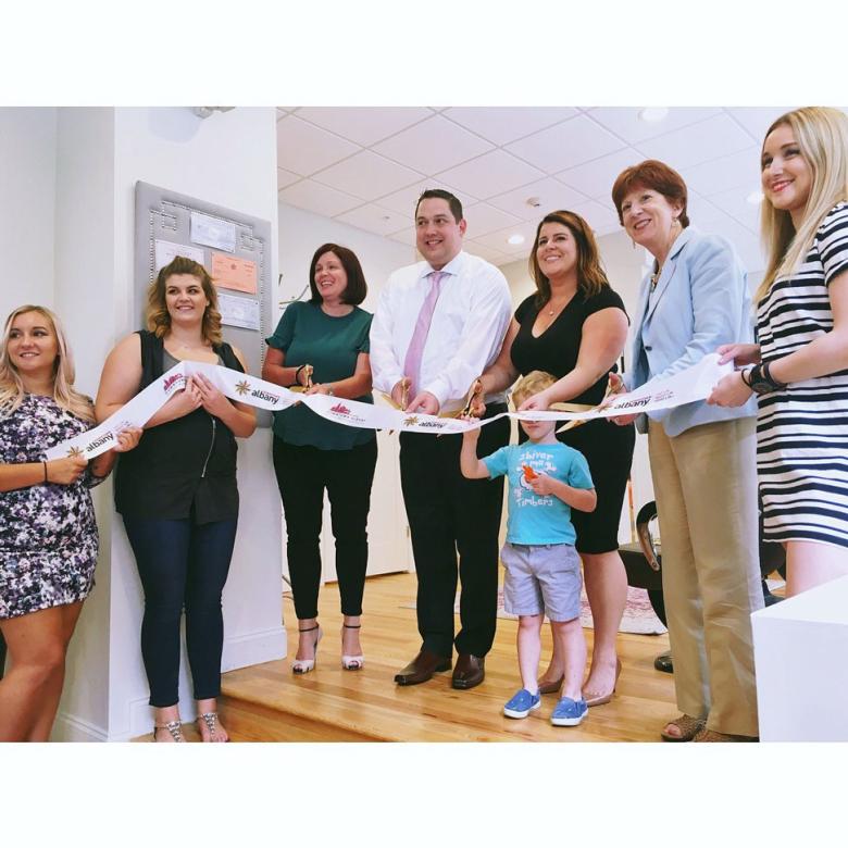 Employees stand with Albany Mayor and BID representatives holding a ribbon for their ribbon cutting ceremony