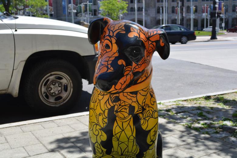 Orange and yellow gradient painted Nipper dog statue with black ink swirl accents sits on the sidewalk in the sun